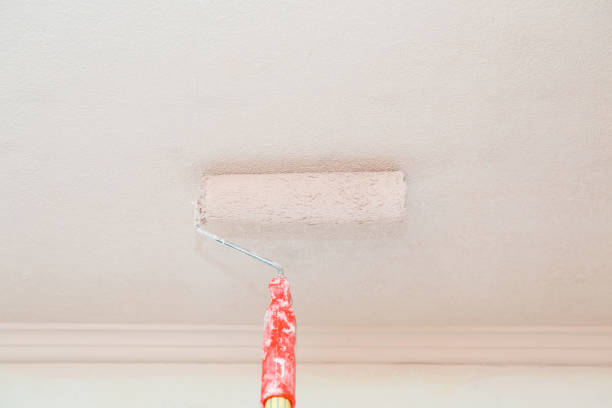 Painting roller on light white pink ceiling wallpaper. Repair work of home. Renovation process. Closeup.