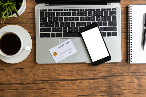 Top view mockup smartphone with blank white screen and computer laptop and credit card on desk