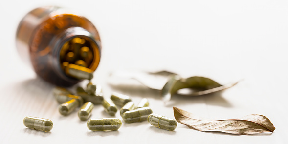 Many nutritional health supplement fish oil capsules spilling out of their bottle onto a white wood table background, shallow depth of focus. Very shallow depth of field with the focus being on one isolated capsule in the foreground of the image. Good copy space.