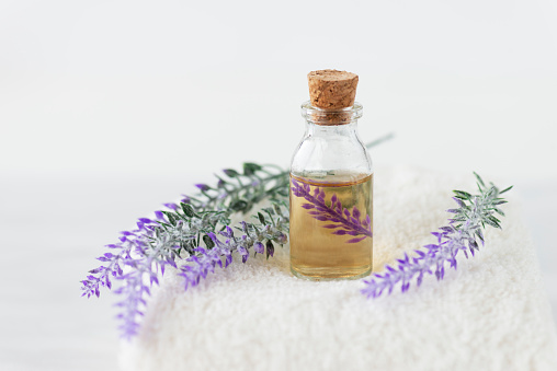 Front view of lavender in oil and  lavender flowers on a white towel on marble background.