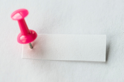 Small white paper pinned with a pink pin on white background.