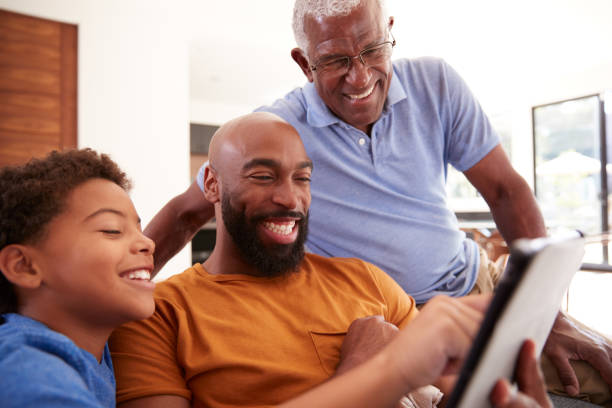 istock Multi-Generation Male African American Family Sitting On Sofa At Home Using Digital Tablet 1263797392