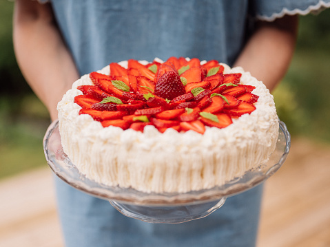 Woman holding strawberry cake outdoors in summer typical cream cake
Traditional cake with cream and strawberries typical for birthdays in summer