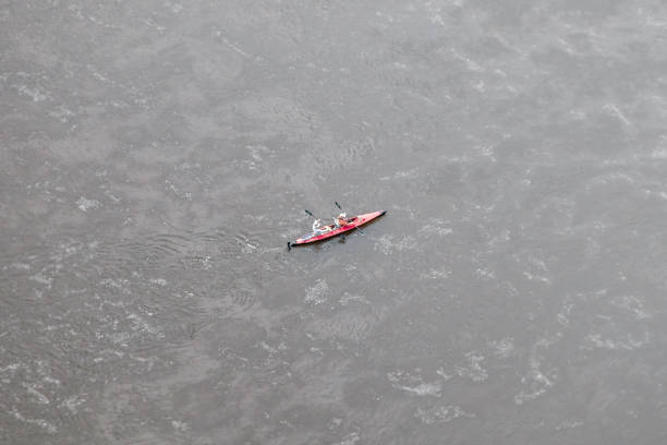 a red kayak with two sporty people with caps on the water from a bird's eye view