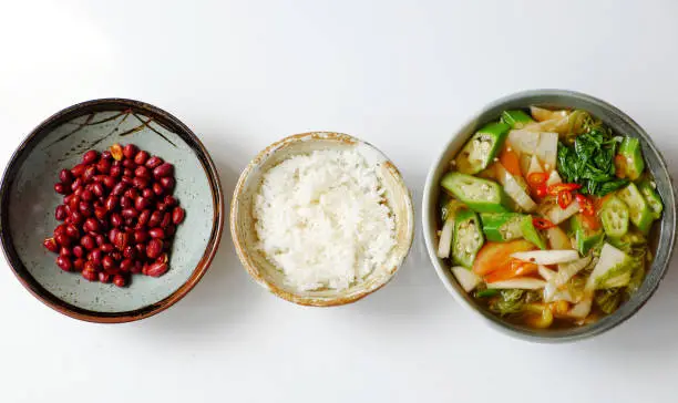 Top view Vietnamese vegan cuisine, daily family meal on white background, vegetables sour soup from tomato, okra, bamboo shoot, water spinach, fried peanut with soy sauce and rice bowl for lunch