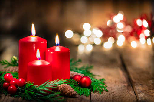 Burning red Advent candle in a warm interior with fireplace.
