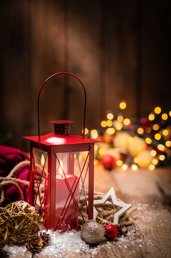 Christmas backgrounds: Christmas red lantern shot on rustic wooden table. The composition is at the bottom of a vertical frame leaving useful copy space for text and/or logo at the top.
String light and Christmas decoration are out of focus at background. Predominant colors are red and brown. High resolution 42Mp studio digital capture taken with Sony A7rII and Sony FE 90mm f2.8 macro G OSS lens