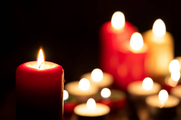 Burning candles in the dark Various lit candles burning in the dark. One candle is on foreground and several are out of focus at background. Predominant colors are red, yellow and black. High resolution 42Mp studio digital capture taken with Sony A7rII and Sony FE 90mm f2.8 macro G OSS lens low lighting stock pictures, royalty-free photos & images