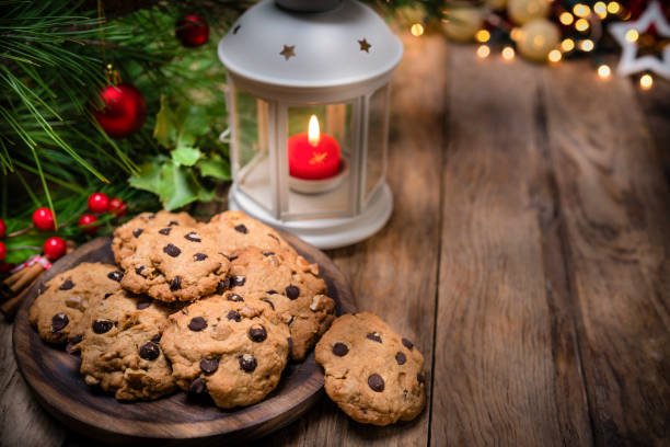 Chocolate cookies for Santa shot on rustic wooden table. Lantern, Christmas ornaments and Christmas lights complete the composition. The composition is at the left of an horizontal frame leaving useful copy space for text and/or logo at the right. Predominant colors are brown and green. High resolution 42Mp studio digital capture taken with SONY A7rII and Zeiss Batis 40mm F2.0 CF lens
