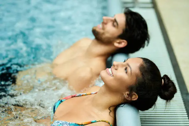 Happy couple leaning their heads at the edge of a pool while relaxing in thermal water at the spa.