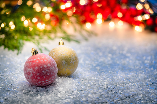 Christmas backgrounds: two Christmas baubles shot on snow with Christmas tree and lights at background. The composition is at the left of an horizontal frame leaving useful copy space for text and/or logo at the right. Predominant colors are red, green and white. High resolution 42Mp studio digital capture taken with Sony A7rII and Sony FE 90mm f2.8 macro G OSS lens