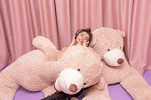 beautiful girl hugging pink big teddy bear soft toy happy smiling on pink background.