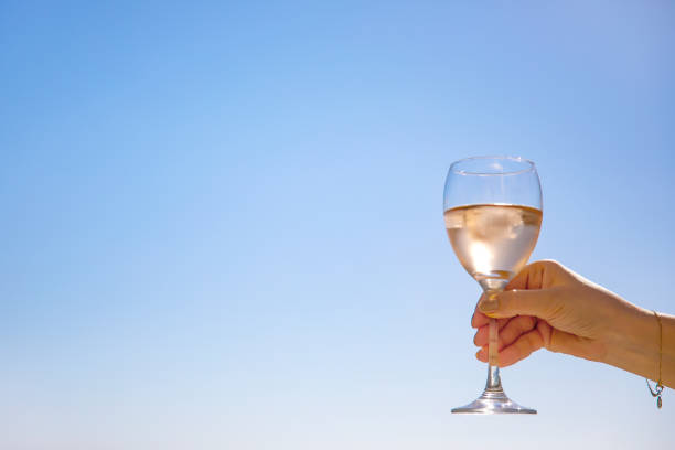 Glass of rose wine in womans hand with sea view and blue sky at background, close-up. Summer day relaxed mood concept