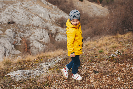 Cute little boy in yellow jacket and cap hiking in the rocky mountains at beautiful autumn day