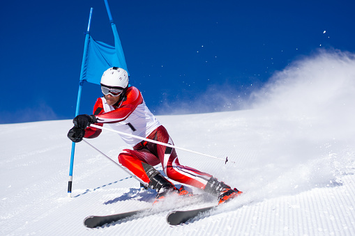 concentrated professional skier ski racer skiing giant slalom touching goal poles on sunny winter day with clear blue sky