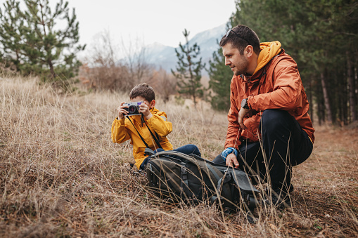 Young father and little son hiking and using camera in nature