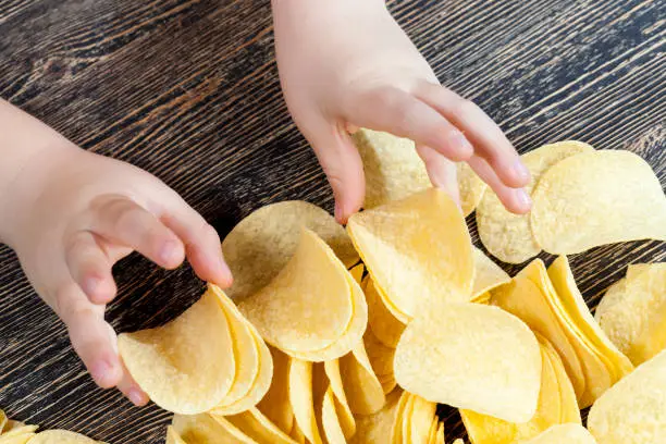 real crispy and salty potato chips ready to eat, close up of unhealthy food products, mashed potato chips in the hand of a child