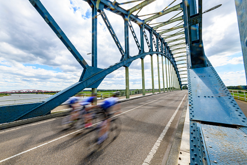 Cyclists riding over the Old IJsselbrug over the river IJssel between Zwolle and Hattem. View from the middle of the road on the old steel arch bridge.