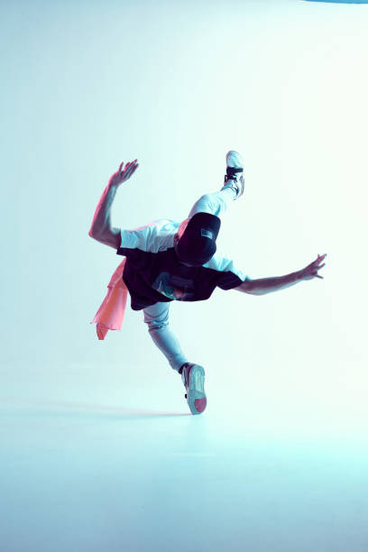 istock Young guy breakdancer performs trick in jump dancing in studio in neon light. Break dance lessons. Dance school poster 1263835274
