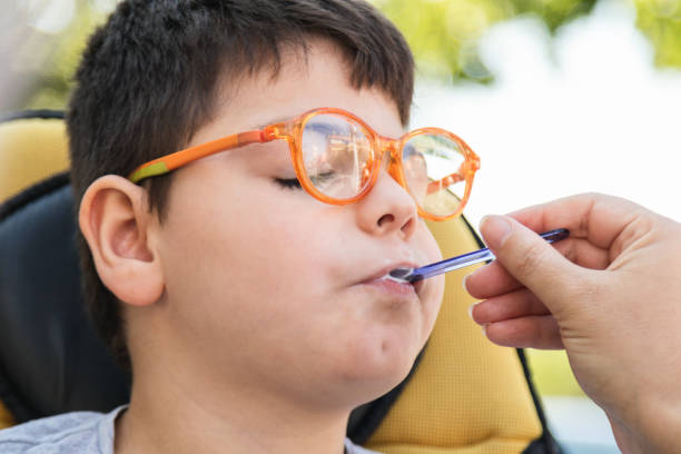 disabled child eating creamy ice cream with a spoon disabled child in wheelchair eating an ice cream with a spoon. woman's hand giving him food. he wears orange glasses and a grey t-shirt. outside kids eating tuna stock pictures, royalty-free photos & images