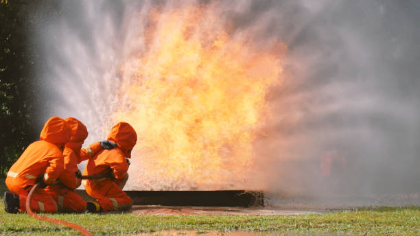 istock Firefighter fighting with flame using fire hose chemical water foam spray engine. Fireman wear hard hat, body safe suit uniform for protection. Rescue training in fire fighting extinguisher 1263837189