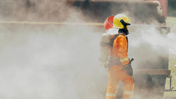 istock Firefighter fighting with flame using fire hose chemical water foam spray engine. Fireman wear hard hat, body safe suit uniform for protection. Rescue training in fire fighting extinguisher 1263837226