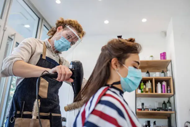 Woman have hair cutting at hair stylist during pandemic isolation, they both wear protective equipment. Hairdresser and customer in a salon with medical masks during virus pandemic. Working with safety mask