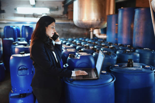 istock Woman using laptop while talking on the mobile phone amongst the drum containers 1263842803