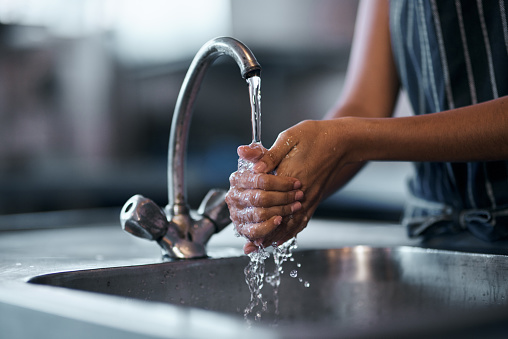 Cropped shot of a  woman washing her hands in the sink of a commercial kitchen
