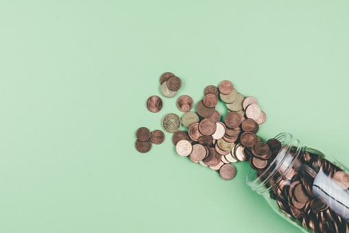 above view of small change Euro coins spilling out of glass jar on green background