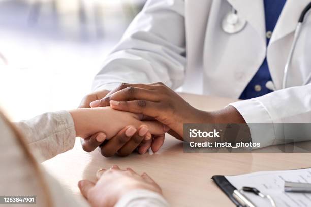 African Female Doctor Hold Hand Of Caucasian Woman Patient Give Comfort Express Health Care Sympathy Medical Help Trust Support Encourage Reassure Infertile Patient At Medical Visit Closeup View Stock Photo - Download Image Now