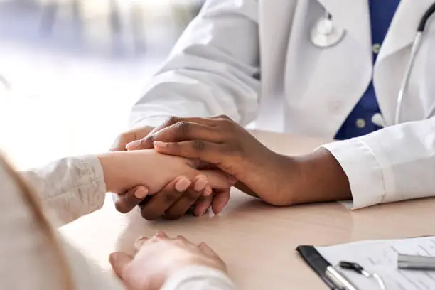 African female doctor hold hand of caucasian woman patient give comfort, express health care sympathy, medical help trust support encourage reassure infertile patient at medical visit, closeup view.