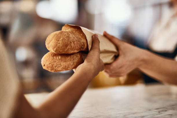 Freshly baked bread, one of life's simplest pleasures Cropped shot of a woman buying freshly made baguettes at a bakery loaf of bread stock pictures, royalty-free photos & images