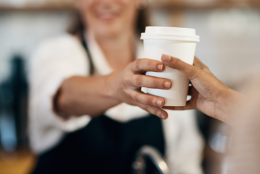 Cropped shot of a barista handing a customer a cup of coffee at a cafe