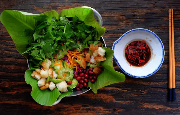 Top view bitter melon salad with violet cabbage, carrot, fried bread, peanut with basil, sour mixed vegetable for vegan cuisine, or diet dish for healthy eating, Vietnamese eating on dark wooden