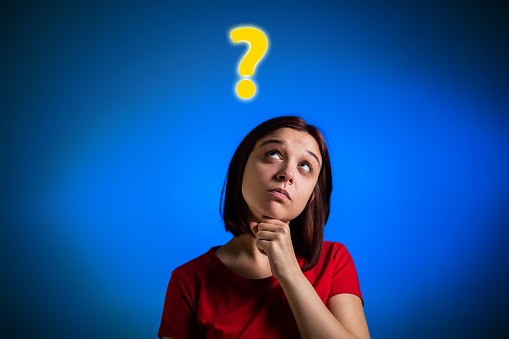 Portrait of young Caucasian woman thinking. Question mark standing over her head. Blue background.
