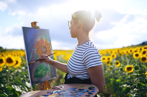side view of female artist paintings sunflowers outdoors.