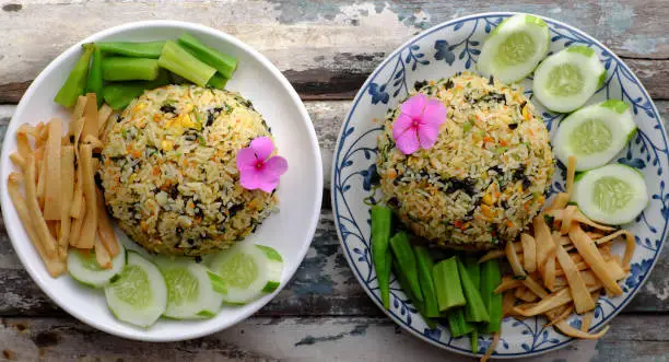 Top view two plate of fried rice dish with vegetables as cucumber, bamboo shoot, okra for family meal at lunch, delicious vegan food ready to eat on wooden background