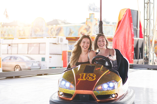 Happy female friends having a fun bumper car ride at the amusement park.