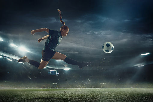 Unstoppable. Female football or soccer player at stadium in flashlight. Young sportive model training, practicing. Moment of attacking, catching. Concept of sport, competition, winning, action, motion, overcoming.