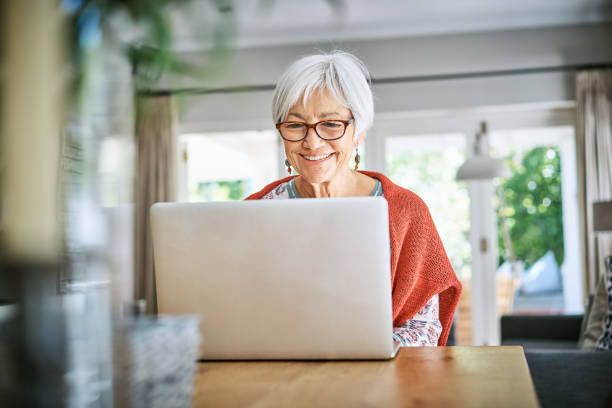 istock Senior woman smiling while sitting at home and working on a laptop 1263871960