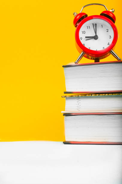 istock clock with books on yellow background 1263873709