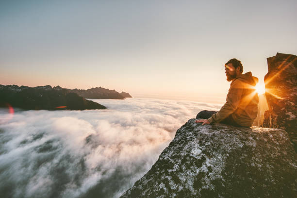 Man relaxing alone on the edge cliff  mountain above clouds travel adventure lifestyle harmony with nature vacations in Norway Man relaxing alone on the edge cliff  mountain above clouds travel adventure lifestyle harmony with nature vacations in Norway senja island photos stock pictures, royalty-free photos & images
