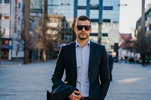 Man in business clothing wearing sunglasses in empty street looking at camera with serious look