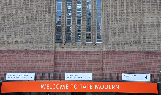 Tate Modern Art gallery on the Southbank of the river Thames, Main Turbine Hall entrance. Orange welcome to the Tate Modern sign. Outdoors on a bright summers day. London, August 2, 2020