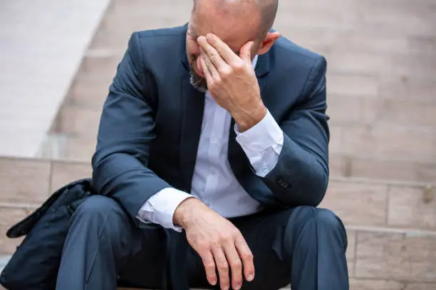 Photo of Depressed businessman sitting on stairs and rubbing his eyes