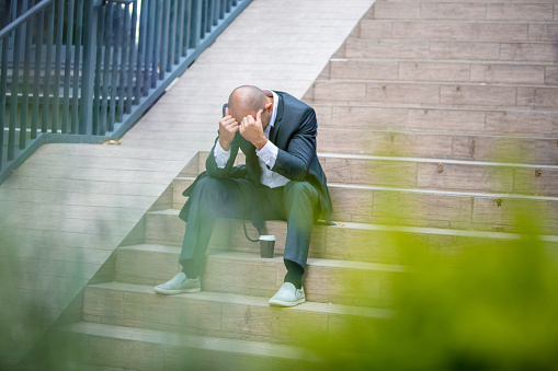 Mid adult businessman, looking stressed, sitting on stairs and having head in his hands