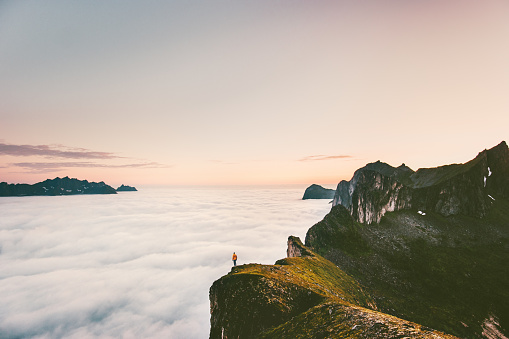 Traveler on the edge cliff mountain above sunset clouds travel adventure lifestyle  journey vacations tranquil landscape in Norway