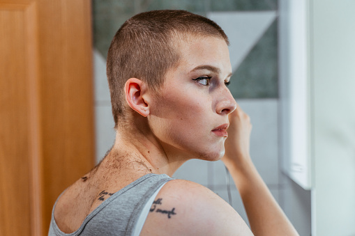 Close up of short haired woman in tank top while cutting her hair