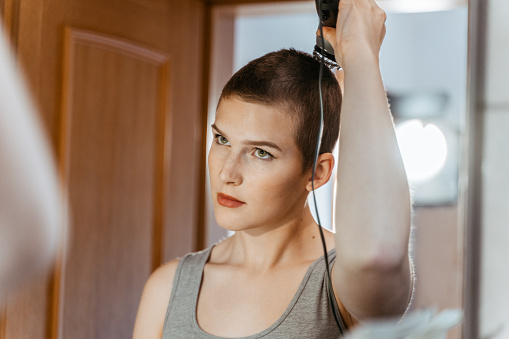 Mirror reflection of short haired woman in tank top using haircutting machine